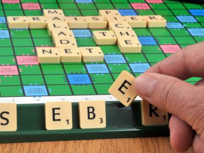 Un homme tient la lettre E du scrabble dans sa main