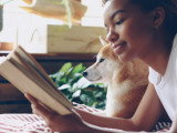 Une femme allongée sur le ventre aux côtés de son chien, et en train de lire un livre