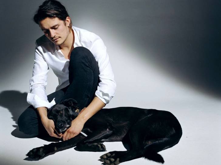 Orlando Bloom assis et en train de caresser son chien Sidi