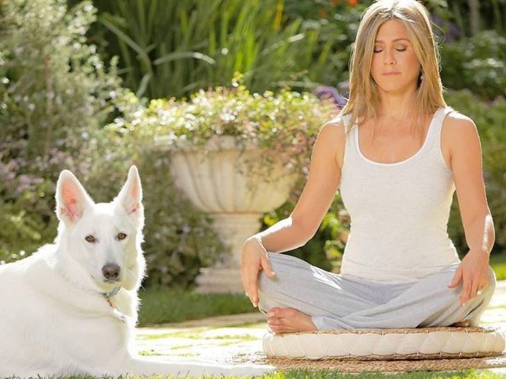 Jennifer Aniston assise en train de méditer, avec son chien Dolly à ses côtés