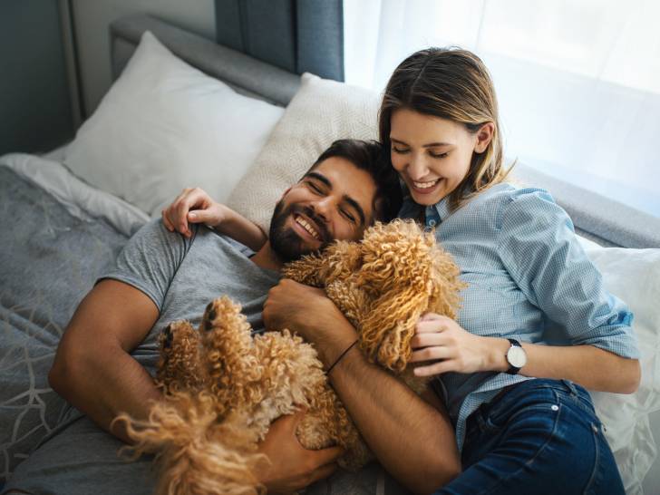 Un couple allongé sur un lit en train de faire un câlin à leur chien