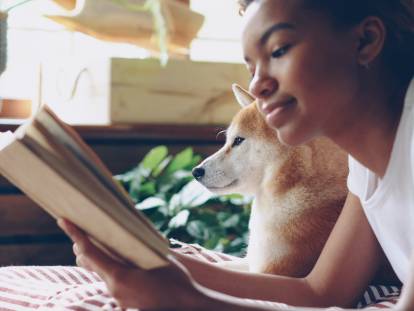 Une femme allongée sur le ventre aux côtés de son chien, et en train de lire un livre