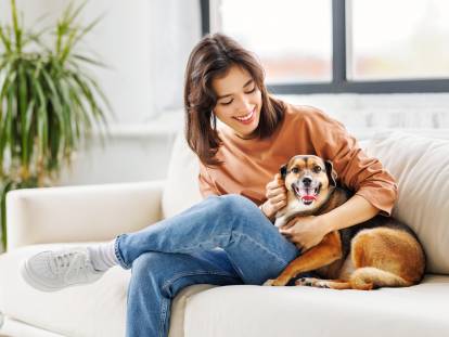 Une femme assise sur un canapé caressant un chien à côté d'elle en souriant