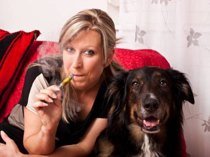 Une femme fume une cigarette électronique à côté de son chien
