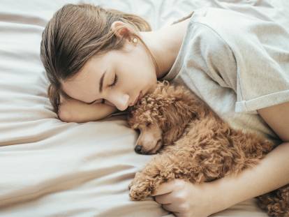Une jeune femme allongée sur un lit et en train de dormir avec son Caniche blotti contre elle