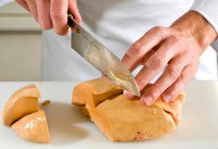 Un cuisinier coupe du foie gras avec un couteau