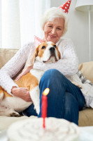 Une dame âgée avec un chapeau pointu d'anniversaire serre son chien dans ses bras