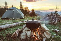 Une marmite pos&eacute;e sur un feu de bois devant une tente de camping