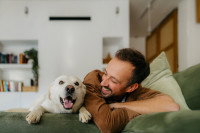 Un chien et un homme assis côte à côte sur un canapé et en train de sourire