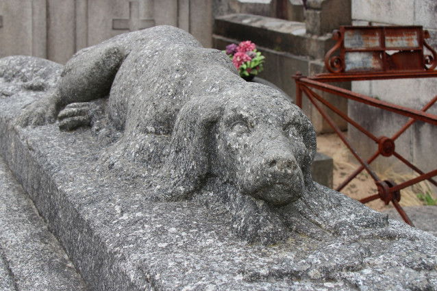 Une sculpture de chien sur une tombe dans un cimetière