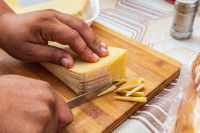 Une femme enlève la croûte du fromage avec un couteau