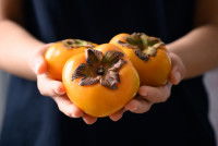 Une femme tient trois kakis dans ses mains