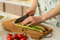 Une femme coupe des asperges sur un support en bois