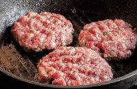 Trois steaks hachés en train de cuire sur un grill