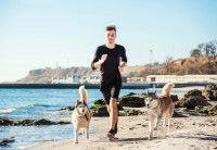 Un jeune homme court sur la plage avec ses deux Huskies Sibériens