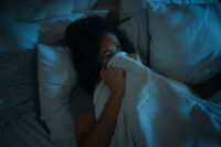 Une femme apeurée allongée dans un lit et se couvrant le visage avec une couette