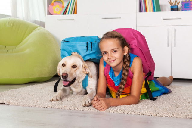 Une petite fille et son chien avec leur cartable allongés dans le salon