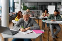 Plusieurs adultes assis en salle de classe et qui écrivent dans leurs cahiers.