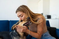 Une femme assise sur un canapé qui embrasse la tête d'un chien
