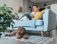 Une femme lisant un livre sur un canapé avec un chien allongé sur un tapis à ses pieds