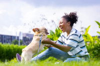 Une femme assise dans l'herbe souriant à un chien qu'elle tient dans ses mains