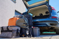 Une voiture garée devant une maison avec le coffre ouvert et des bagages à côté