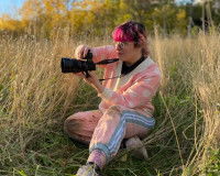Roxane Lasseur assise dans des herbes hautes et en train de prendre une photo