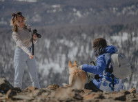 Une photographe professionnelle en train de prendre en photo un chien et son maître dans un paysage naturel