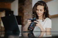 Une photographe professionnelle installée devant son ordinateur portable et en train de manipuler son appareil photo
