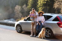 Une famille et son chien adossés à une voiture