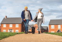 Un jeune couple en train de promener son chien, avec en arrière-plan des maisons en brique