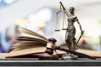 Zoom sur un livre, une statue de la justice et un maillet qui sont posés sur une table