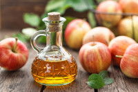 Du vinaigre de cidre et des pommes posés sur une table en bois