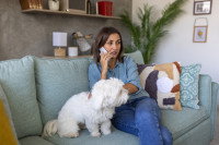 Une femme assise sur un canapé avec son chien et parlant au téléphone