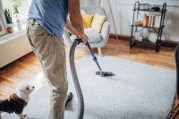 Un homme passant l'aspirateur dans son salon avec son chien à côté