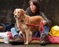 Une femme sans-abri assise dans la rue avec son chien en laisse