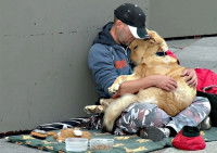Un homme sans-abri assis dans la rue avec son chien sur les genoux, et en train de lui faire un câlin