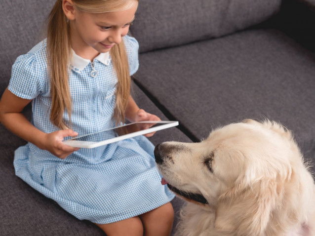 Une petite fille tient une tablette dans ses mains aux côtés de son chien