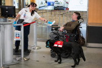Une employée tendant un papier à un homme en fauteuil roulant accompagné d'un chien d'assistance