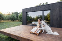 Un Golden Retriever assis et appuyé sur sa maîtresse, sur la terrasse d'une maison en bois.
