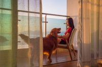 Une femme et son chien sur un balcon face à la mer.