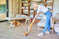 Une femme passant l'aspirateur dans le salon, tandis que son chien est allongé et la regarde.