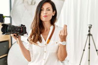 Une photographe tenant un appareil dans la main et faisant le symbole de l'argent avec l'autre