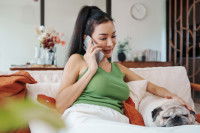 Une femme assise sur un canapé passant un appel, avec un chien à ses côtes