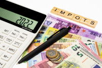 Des billets, une calculatrice et le mot impôt en lettres de bois