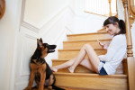 Un chiot Berger Allemand observant une jeune femme souriante assise dans un escalier en bois