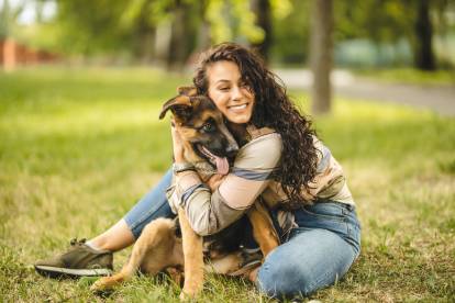 Un Berger Allemand assis et tenu tendrement par une femme dans un parc verdoyant.