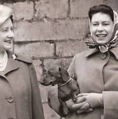 La reine Elizabeth II en train de tenir un Teckel dans ses bras et de sourire