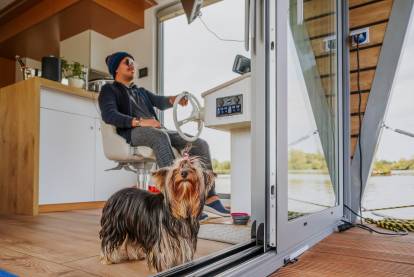 Un Yorkshire Terrier regardant à travers la baie vitrée d'un bateau, que son maître conduit en arrière-plan