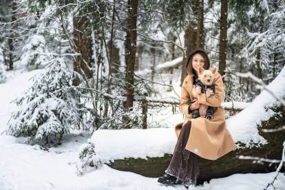 Une femme assise sur un tronc d'arbre dans une forêt enneigée avec un Yorkshire Terrier dans les bras